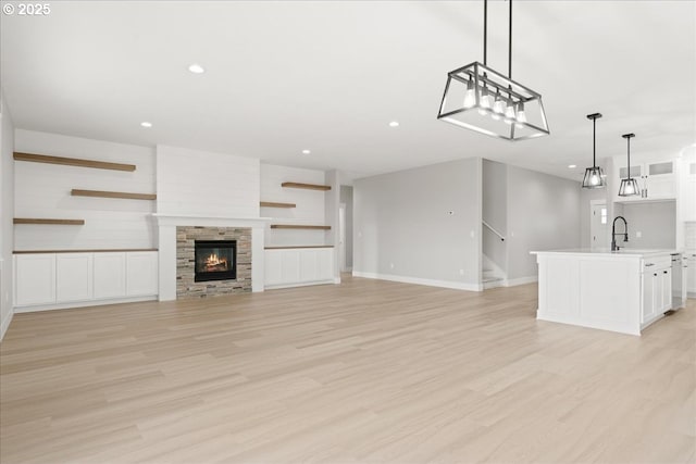 unfurnished living room with a stone fireplace, recessed lighting, baseboards, stairway, and light wood-type flooring