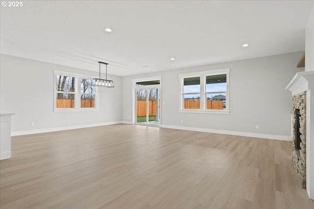 unfurnished living room featuring light wood finished floors, a stone fireplace, recessed lighting, and baseboards