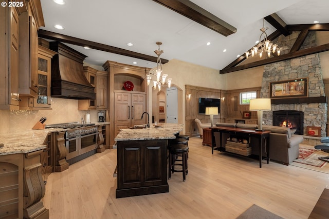 kitchen with beamed ceiling, double oven range, light wood-style floors, a stone fireplace, and custom exhaust hood