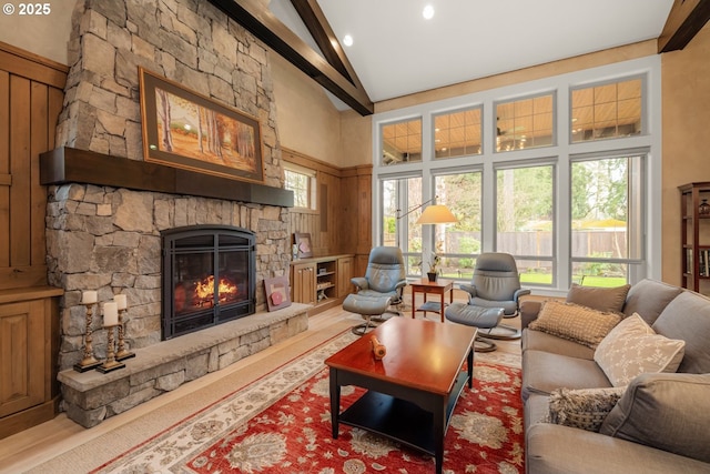 living area with a stone fireplace, beamed ceiling, wood finished floors, and high vaulted ceiling