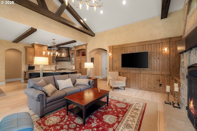 living area featuring a chandelier, beam ceiling, a warm lit fireplace, arched walkways, and high vaulted ceiling