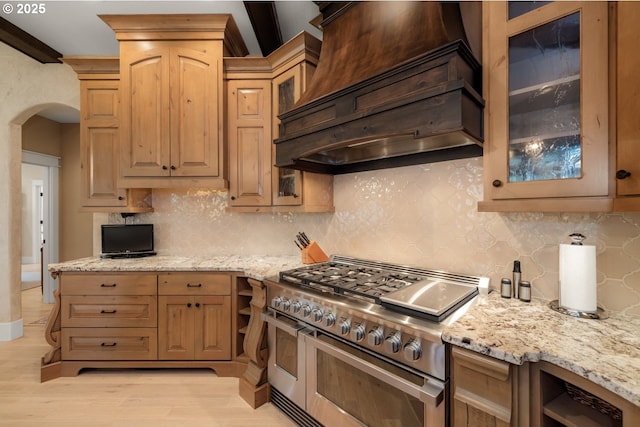 kitchen with light wood-type flooring, double oven range, arched walkways, decorative backsplash, and custom exhaust hood