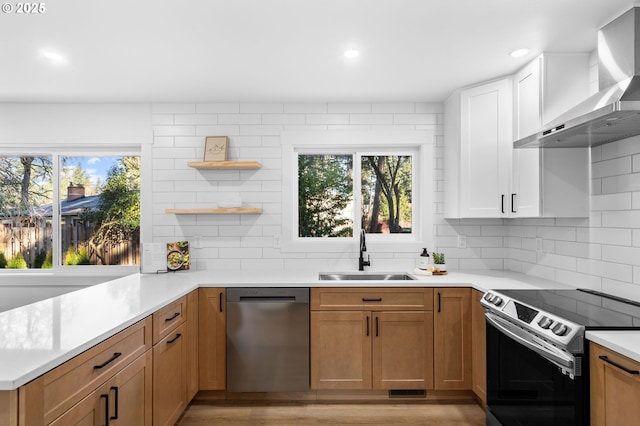 kitchen featuring kitchen peninsula, appliances with stainless steel finishes, wall chimney exhaust hood, sink, and white cabinetry