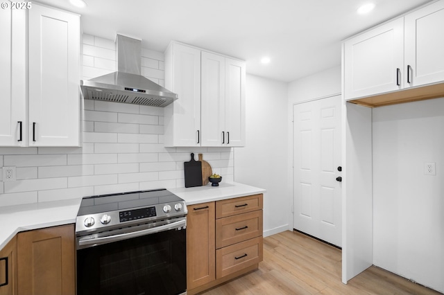 kitchen featuring stainless steel range, light wood-type flooring, white cabinets, and wall chimney exhaust hood