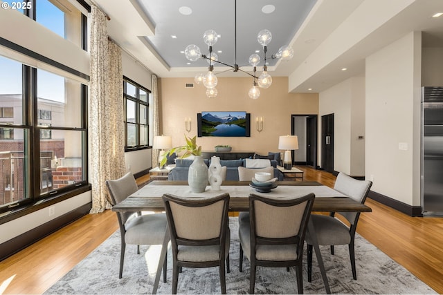 dining room with light wood-type flooring, baseboards, visible vents, and a tray ceiling