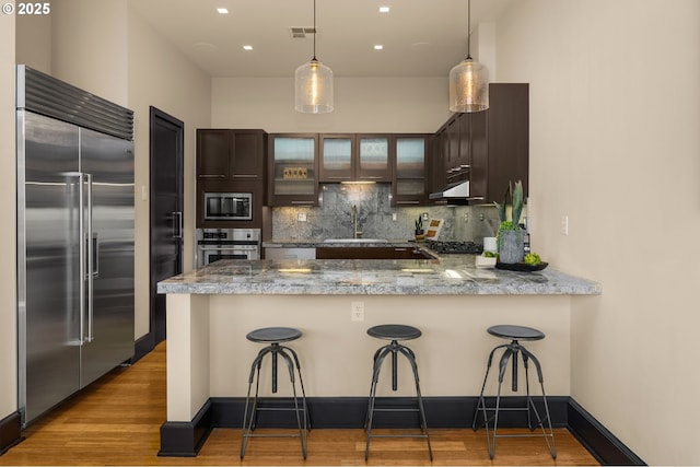 kitchen with built in appliances, a peninsula, a sink, visible vents, and decorative backsplash