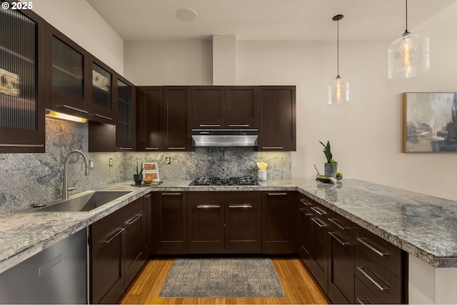 kitchen with tasteful backsplash, light wood-style floors, under cabinet range hood, gas cooktop, and a sink