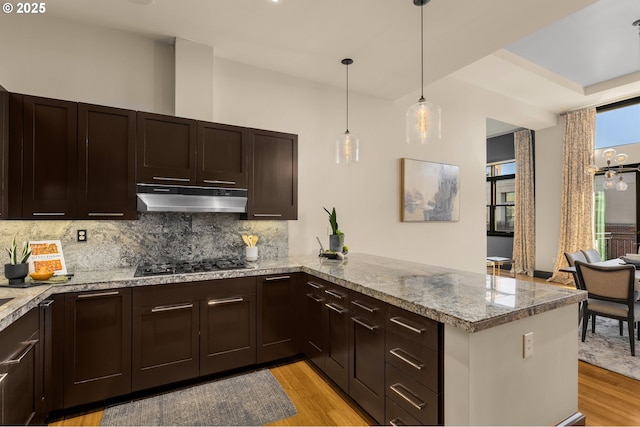 kitchen featuring black gas cooktop, light wood-style floors, under cabinet range hood, and a peninsula