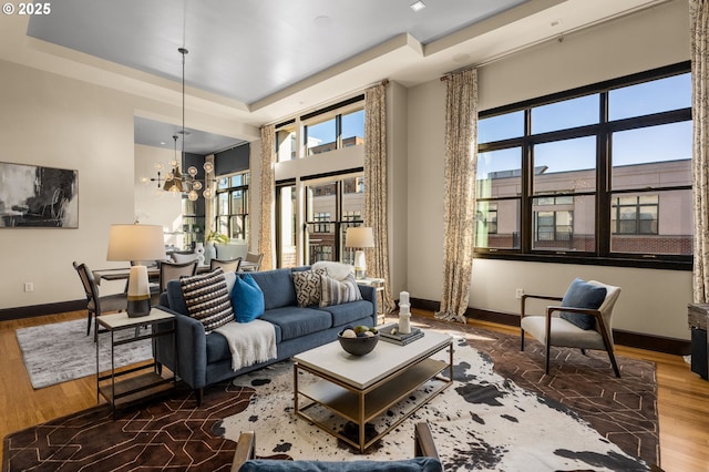 living room featuring a raised ceiling, baseboards, an inviting chandelier, and wood finished floors