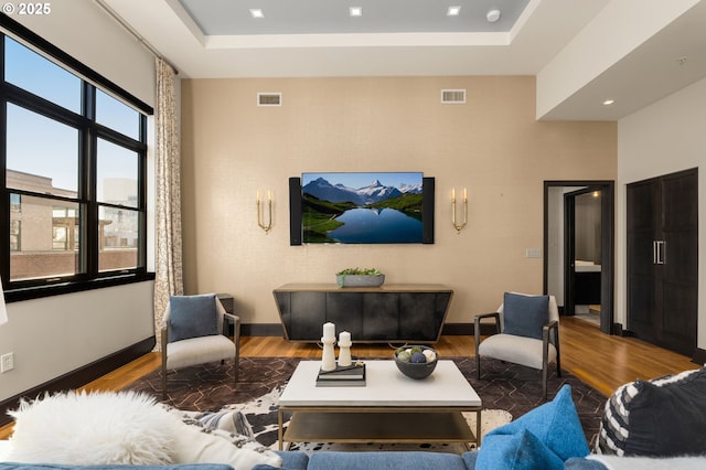 living room featuring baseboards, visible vents, a raised ceiling, and wood finished floors