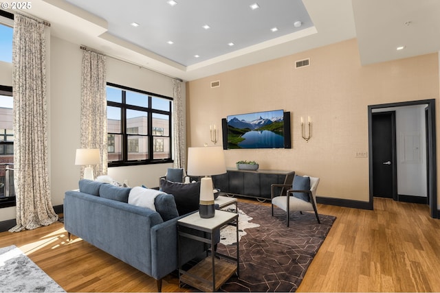 living room featuring a tray ceiling, light wood-type flooring, visible vents, and baseboards