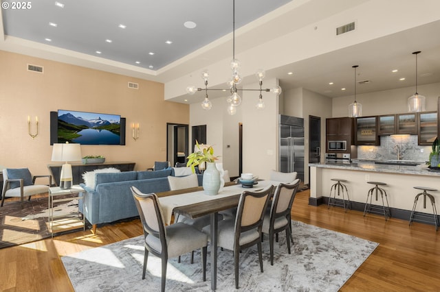 dining room with recessed lighting, a raised ceiling, visible vents, a high ceiling, and wood finished floors