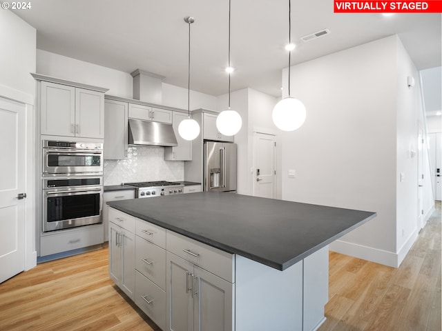 kitchen featuring pendant lighting, stainless steel appliances, dark countertops, a kitchen island, and under cabinet range hood