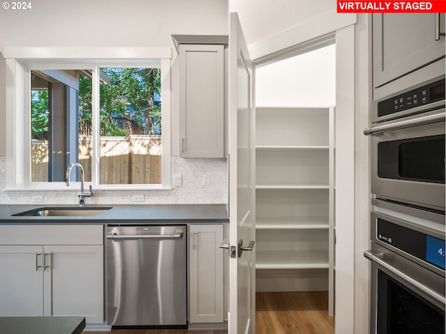 kitchen featuring decorative backsplash, dark countertops, wood finished floors, stainless steel appliances, and a sink