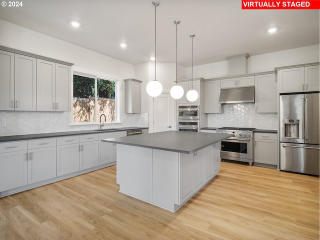 kitchen with premium appliances, dark countertops, decorative light fixtures, under cabinet range hood, and a sink