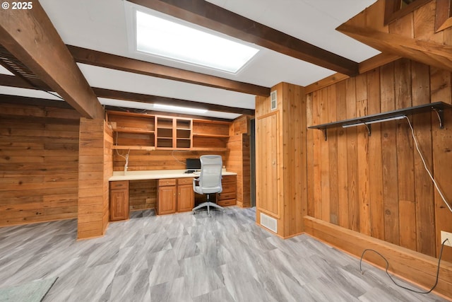 unfurnished office with built in desk, beamed ceiling, wood walls, and light hardwood / wood-style flooring