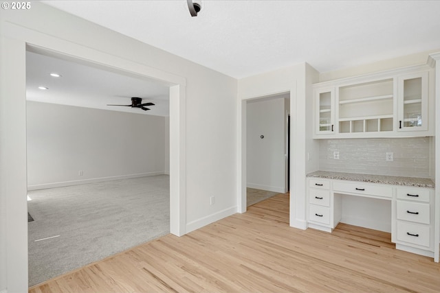 9240 SW Stono Dr, Tualatin, OR 97062 - kitchen with light stone counters, a ceiling fan, white cabinetry, glass insert cabinets, and tasteful backsplash