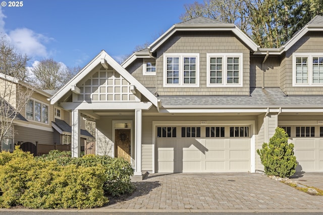 view of front facade featuring decorative driveway, a garage, and a shingled roof