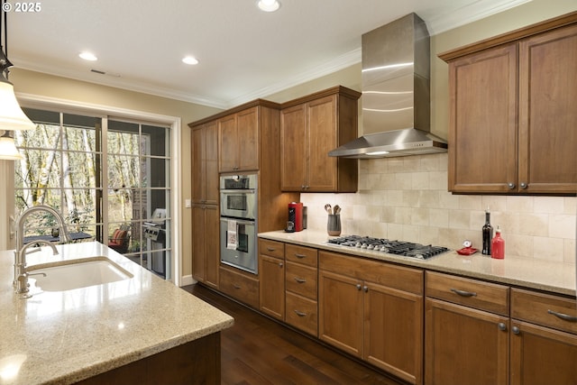 kitchen with brown cabinets, ornamental molding, a sink, stainless steel appliances, and wall chimney range hood