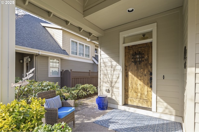 property entrance with a patio, fence, and roof with shingles