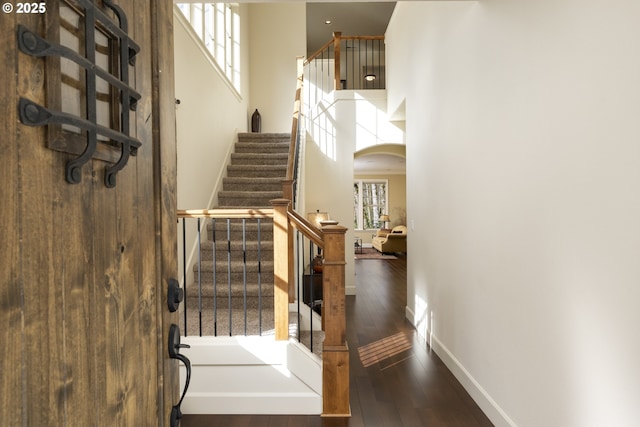 stairs featuring a high ceiling, a wealth of natural light, arched walkways, and wood-type flooring