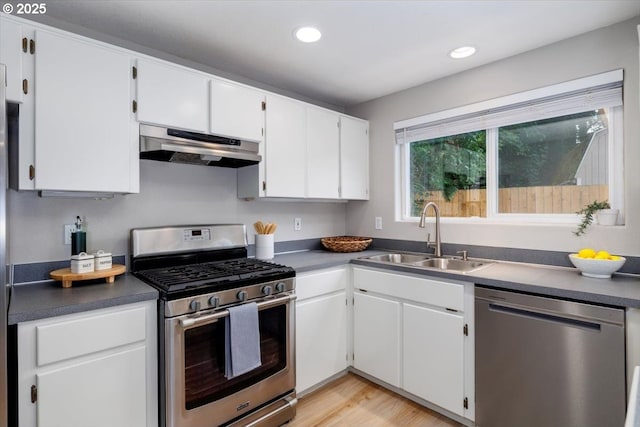 kitchen featuring appliances with stainless steel finishes, a sink, under cabinet range hood, dark countertops, and white cabinetry