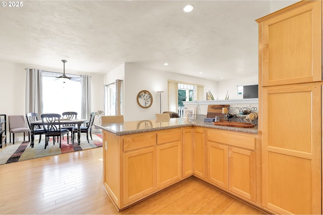 kitchen with light brown cabinetry, kitchen peninsula, light hardwood / wood-style floors, and hanging light fixtures