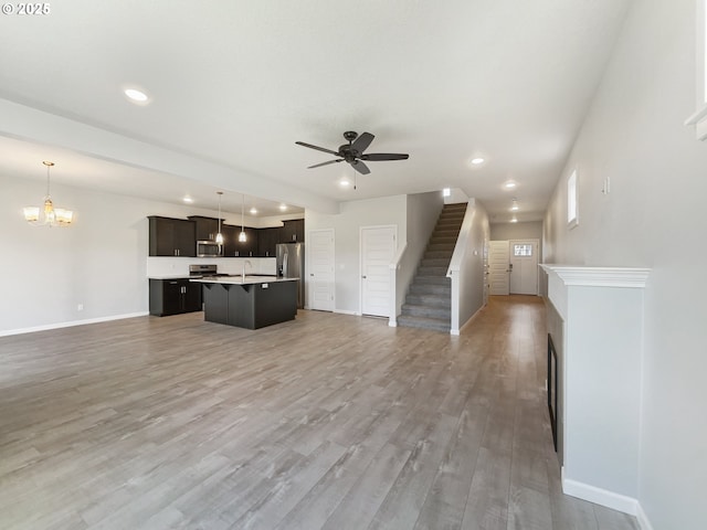 unfurnished living room featuring ceiling fan with notable chandelier, recessed lighting, stairway, a sink, and baseboards