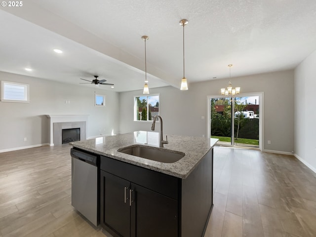 kitchen with an island with sink, a fireplace, dishwasher, a sink, and open floor plan