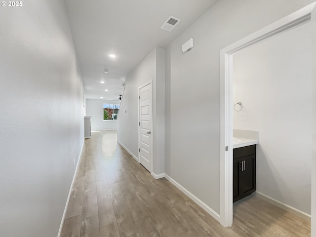 corridor with light wood finished floors, baseboards, visible vents, and recessed lighting