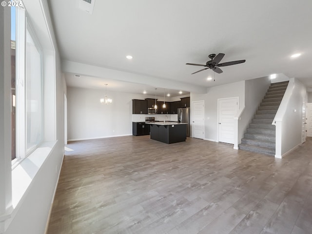 unfurnished living room with baseboards, a sink, ceiling fan with notable chandelier, recessed lighting, and stairs