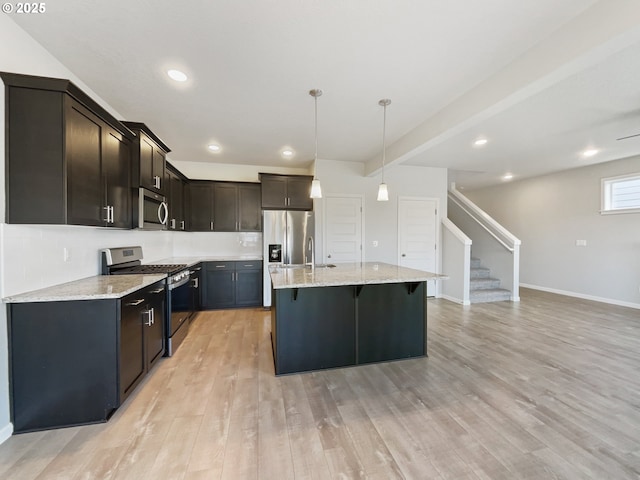 kitchen featuring light stone countertops, a kitchen bar, a kitchen island, stainless steel appliances, and light wood finished floors