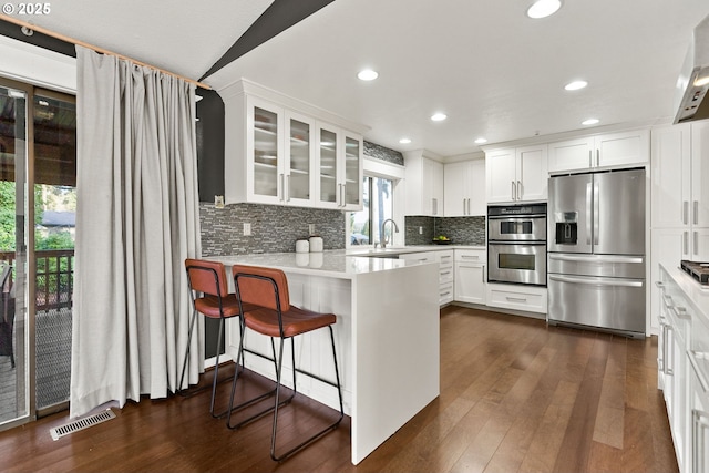 kitchen featuring visible vents, white cabinets, glass insert cabinets, appliances with stainless steel finishes, and a peninsula