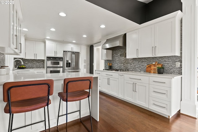 kitchen featuring wall chimney exhaust hood, white cabinetry, stainless steel appliances, and light countertops