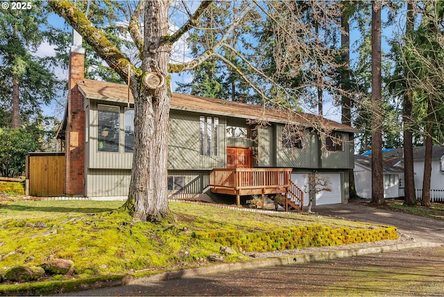 bi-level home with driveway, an attached garage, a chimney, and a wooden deck