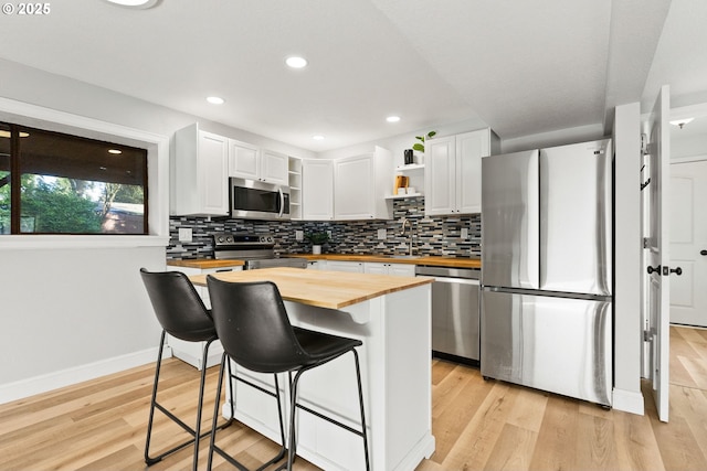 kitchen with a breakfast bar area, white cabinetry, wooden counters, appliances with stainless steel finishes, and open shelves