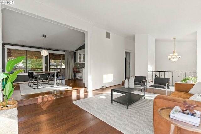 living area with a chandelier, lofted ceiling, visible vents, and wood finished floors