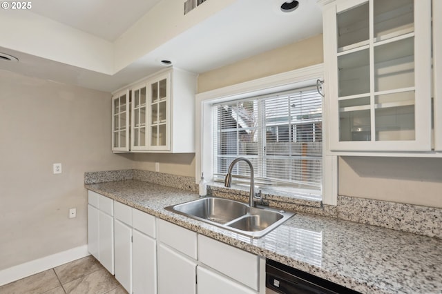 kitchen featuring dishwasher, sink, white cabinetry, light tile patterned floors, and light stone counters