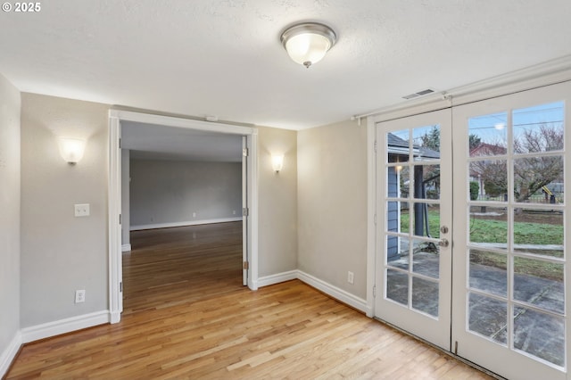 empty room with light hardwood / wood-style floors, a textured ceiling, and french doors