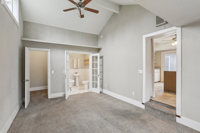 unfurnished bedroom featuring connected bathroom, light carpet, french doors, ceiling fan, and beam ceiling