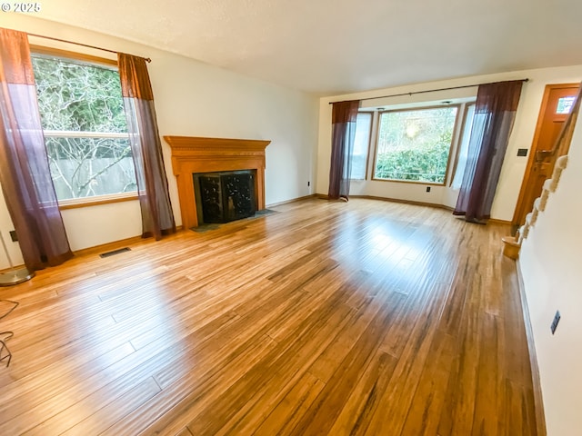 3241 SW Spring Garden St, Portland, OR 97219 - unfurnished living room with light wood-style flooring, a fireplace with flush hearth, and stairs