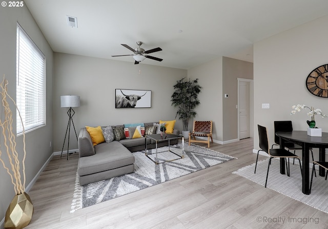 living room featuring light wood-type flooring, baseboards, visible vents, and ceiling fan