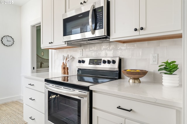 4633 SE 35th Ave Unit B, Portland, OR 97202 - kitchen with stainless steel appliances, decorative backsplash, white cabinets, light stone countertops, and baseboards