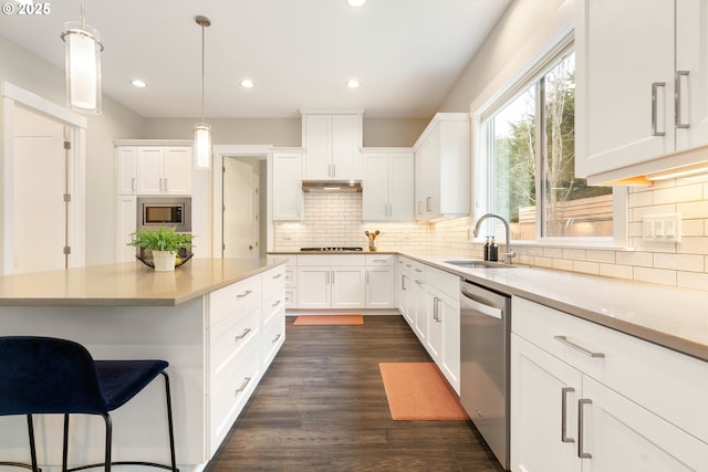 kitchen featuring dark wood-type flooring, light countertops, stainless steel appliances, white cabinetry, and a sink