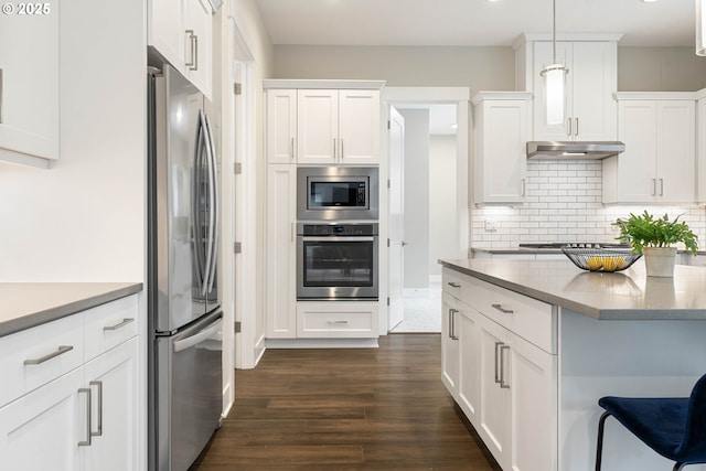 kitchen with under cabinet range hood, decorative backsplash, appliances with stainless steel finishes, dark wood-style floors, and white cabinets