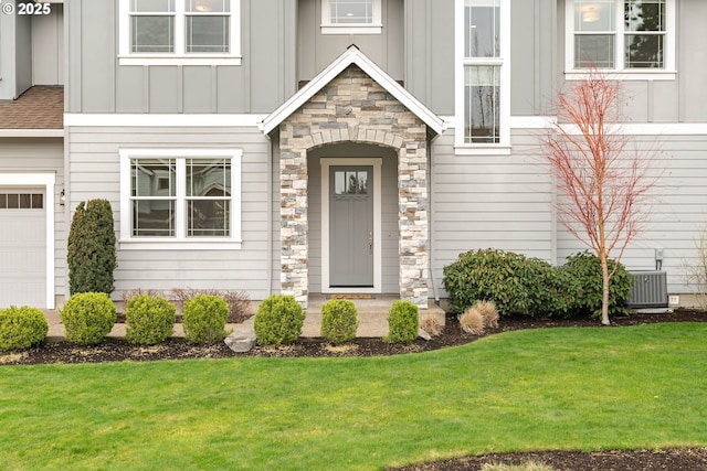 entrance to property featuring cooling unit, board and batten siding, stone siding, and a yard