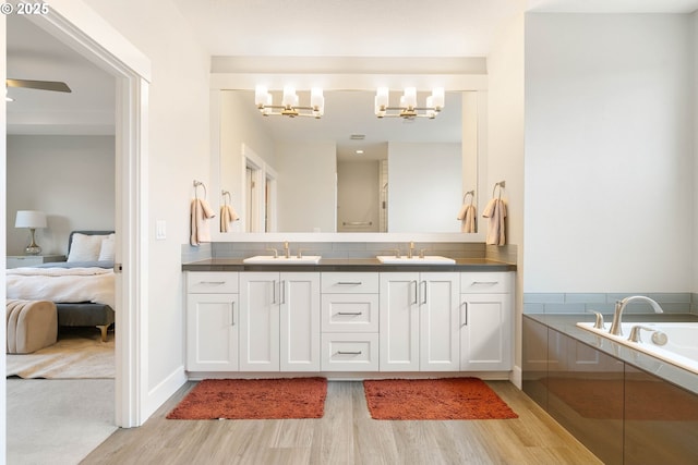 ensuite bathroom featuring a sink, a notable chandelier, wood finished floors, and double vanity