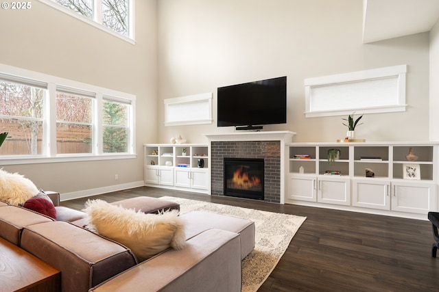 living area featuring a high ceiling, baseboards, dark wood-type flooring, and a brick fireplace