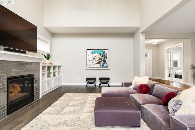 living room featuring a brick fireplace, dark wood-style floors, baseboards, and a towering ceiling