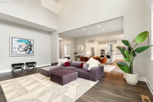 living area featuring baseboards, visible vents, recessed lighting, dark wood-style flooring, and a towering ceiling